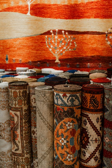 Close-up view of two traditional patterned rugs with intricate geometric and floral designs in red, blue, and beige tones, draped over a white textured wall with visible wear and stains. One rug cover